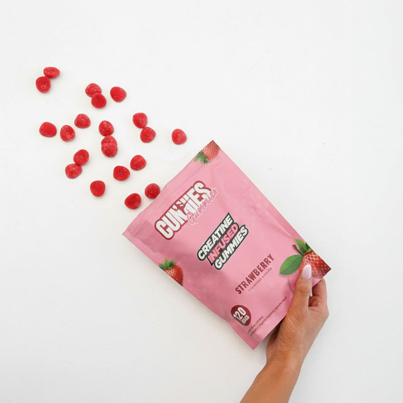 Hand holding an open bag of Strawberry Cunnies creatine gummies with gummies spilling out